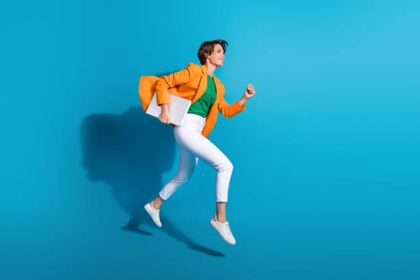 Profile side photo of excited cheerful active lady wear stylish orange clothes go fast empty space isolated on blue color background stock photo