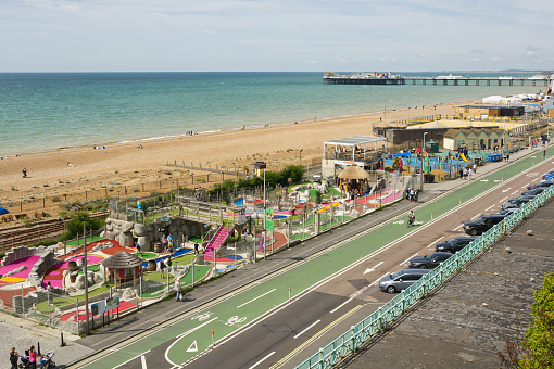 Mini-golf, children's playground and volleyball court on the Beach at Brighton in East Sussex, England. With Palace Pier in background and people enjoying the seaside.