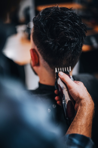 Barber cutting man's hair, close-up of electric razor.