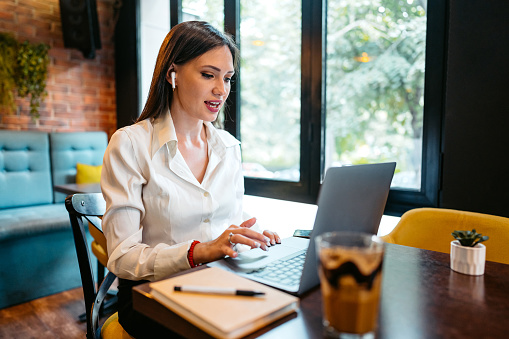 Young beautiful businesswoman having a video call on laptop in a café.