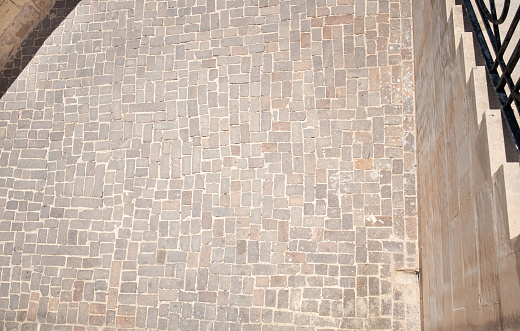 Top view of historic cobblestone pavement made of brown stones. On the side the edge of a stairway leading up. There is space for text.