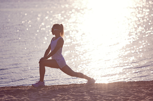 Full length portrait of beautiful sportive girl training at sunrise over seaside. Sportswoman training on beach. Morning fitness workout. Concept of sport, recreation, healthy lifestyle, hobby.