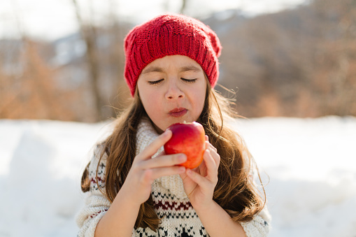 Little girl walking on the snow and eating apple fruit as a snack in nature