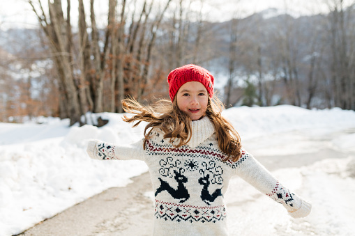 Playful girl walking on a road with snow in nature , wearing red hat