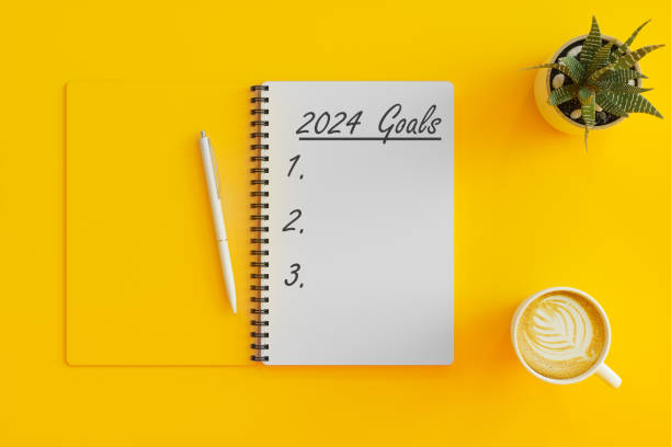 concept des objectifs du nouvel an 2024. vue à angle élevé de la liste des objectifs 2024 avec cahier, tasse à café et plante succulente sur fond jaune - voeux 2024 photos et images de collection