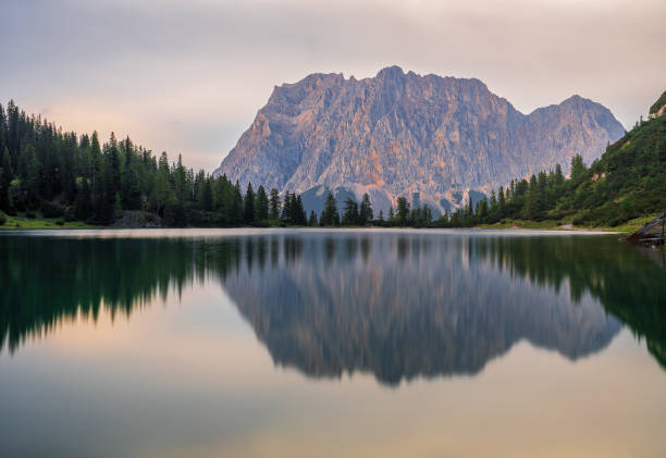 Mount Zugspitze mirrored in Lake Seebensee with clouds covering the mountain partially
