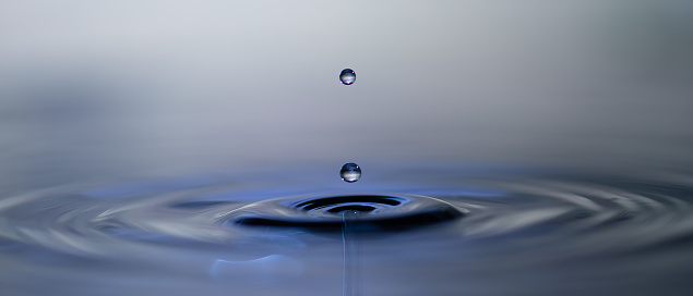 Close-up of water drops falling on rippled water.