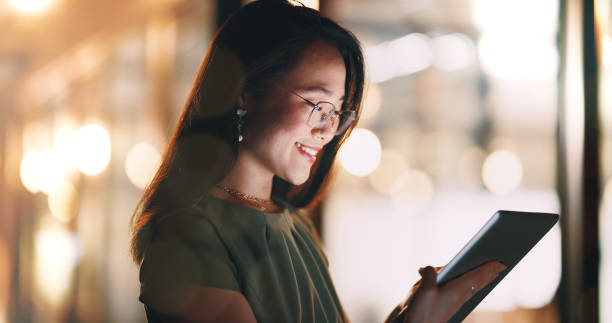 istock Asian woman, tablet and typing in night office while working on project deadline. Digital tech, touchscreen and happy business woman working late in dark workplace, researching and writing email. 1652687865