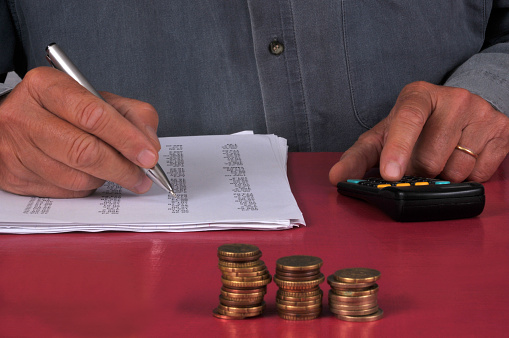 Accounting concept with a man doing calculations with a stack of coins in the foreground
