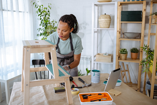 A mid adult woman is painting wooden furniture and enjoying the hobby