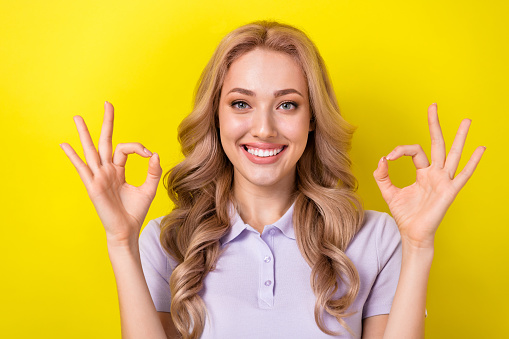 Portrait of cheerful positive woman with wavy hairdo dressed purple t-shirt showing okey approve isolated on yellow color background.