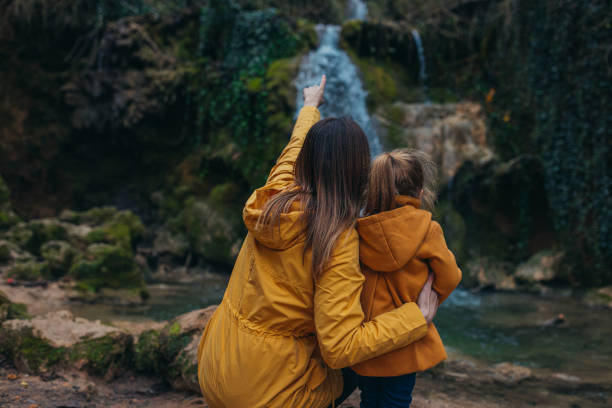 A woman pointing on waterfall with her hand with a child standing beside her.