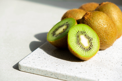 Ripe kiwi fruits in sunlight. Heap of whole kiwi fruits and fresh cut kiwi on table. Healthy organic fruits full of vitamins and antioxidants. Green diet.