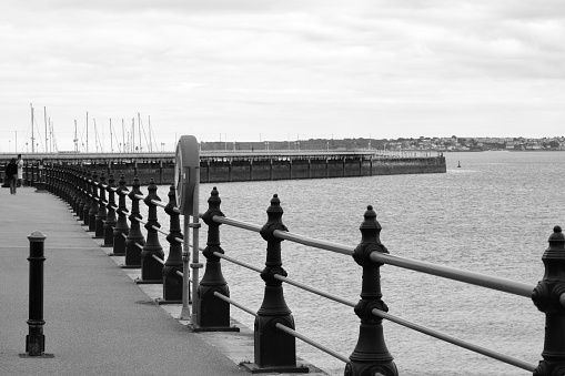 A black and white image of a section of  the long seafront at Torquay with its promenades, stepped sea walls, walkways and railings.