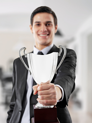 Businessman holding a trophy and looking at camera in a modern office
