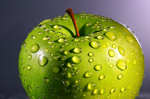 Glistening apple with a captivating water droplet, illuminated in a dramatic play of light and shadow. A stunning blend of nature's beauty and artistic lighting.