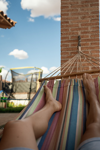Unrecognizable person relaxing in a hammock. Vertical point of view shot of the legs of an anonymous young man lying in a hammock in the backyard swinging slowly.