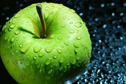 Glistening apple with a captivating water droplet, illuminated in a dramatic play of light and shadow. A stunning blend of nature's beauty and artistic lighting.