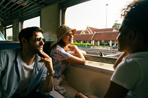Group of Happy Diversity people friends travel in Thailand on local train. Man and woman tourist travel on railroad transportation on summer holiday vacations.