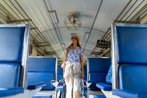 Caucasian woman tourist travel in Thailand on local train. Attractive girl tourist looking for seat on the train during travel on railroad transportation on summer holiday vacations.