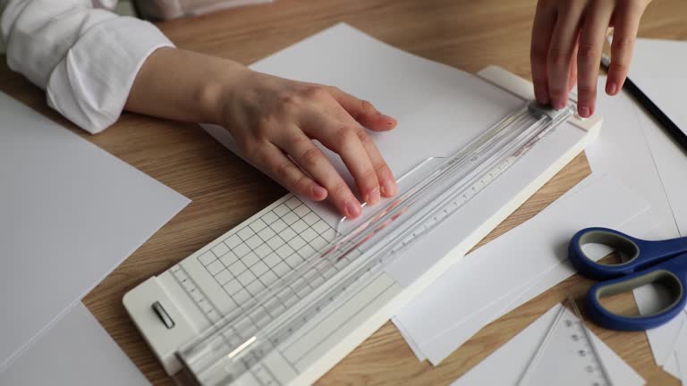 Person uses manual paper cutting device at office desk