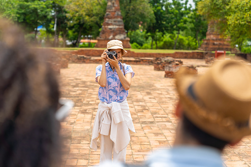 Group of Diversity people friends tourist using digital camera taking picture together during travel architecture and old ruin temple famous place in Ayutthaya Province, Thailand on summer holiday vacation.