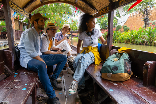 Group of Diversity people traveler and local tour guide travel floating market by traditional wooden boat in canal during travel Ayutthaya Province in Thailand on summer holiday vacation.