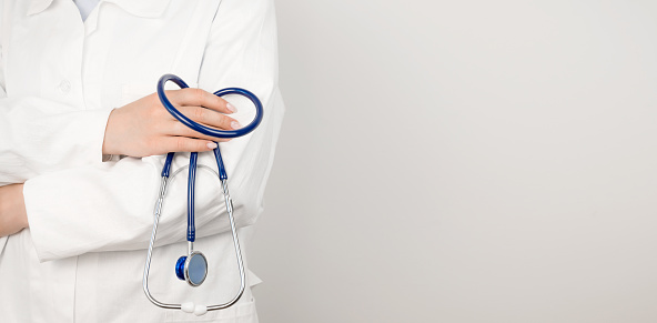A doctor in a white medical coat holds a stethoscope in his hands. Healthcare concept. Banner with place for text