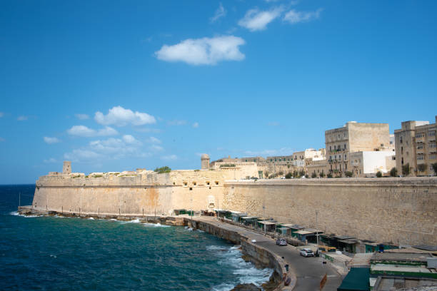 a muralha do forte st. elmo em malta em valletta. ao fundo, o céu azul e as nuvens. em primeiro plano o mar e uma praia. - st elmo - fotografias e filmes do acervo