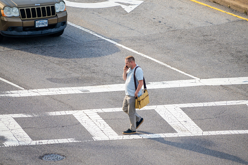 Norfolk Virginia - August 21 2023: A Man Crossing the Street While Talking on a Cell Phone with Traffic Waiting at the Light
