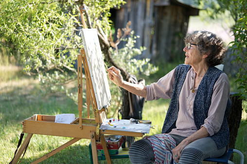 Portrait of a senior painter holding palette with a brush and looking away. Artist in his studio.