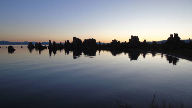 the iconic tufa rock formations of mono lake are reflected in silhouette on the water's surface at dawn. - mono county imagens e fotografias de stock