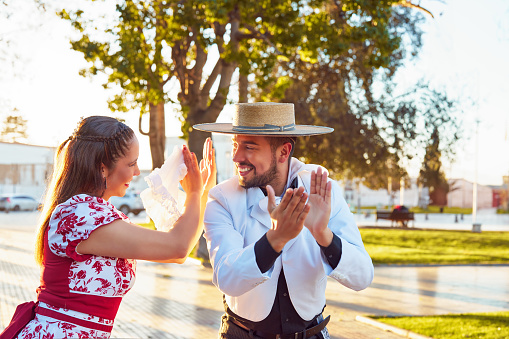 portrait young couple dressed in traditional huaso clothing clapping to the rhythm of the cueca dance outdoors