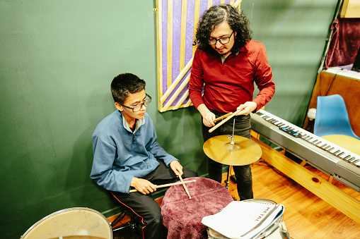 Mid adult man teaching drum kit to his student at a recording studio