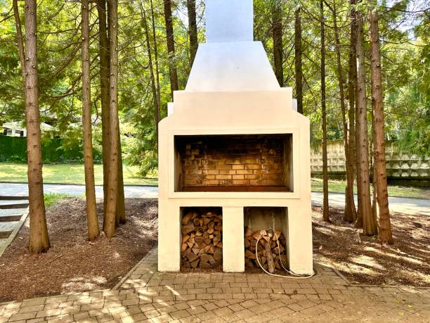 An open brick oven, a barbecue for cooking kebabs and other dishes on fire among pine trees in the park on a gazebo on a sunny day. Summer kitchen with pizza oven and barbecue grill. Cooking food on wood burning in the oven. Open oven.