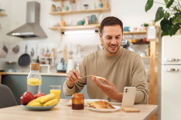 istock Young casually clothed man using phone while having breakfast in a domestic kitchen 1652943815