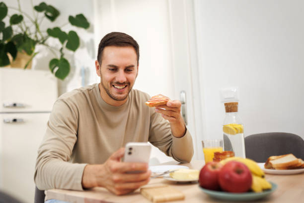 istock Young casually clothed man text messaging while having breakfast in a domestic kitchen 1652944922