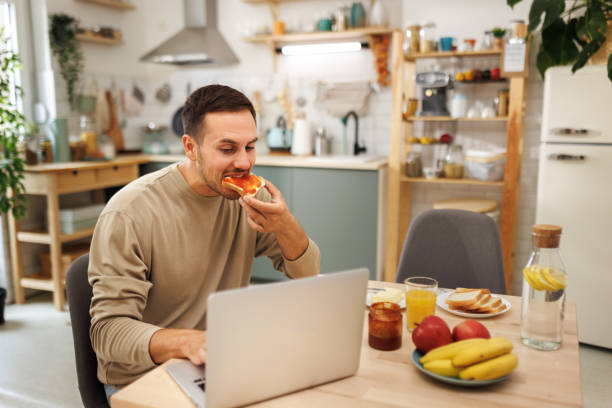 istock Young casually clothed man using laptop while having breakfast in a domestic kitchen 1652944928