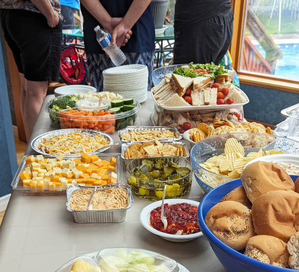 Young family members stand near a kitchen table filled with a variety of food for a potluck party.