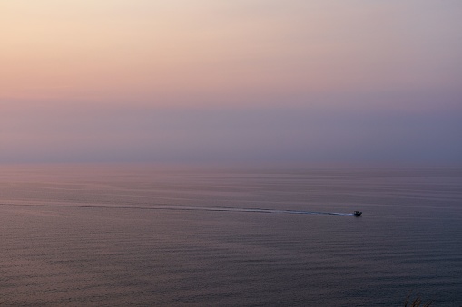 An aerial view of a small vessel sailing in a tranquil bay at sunset