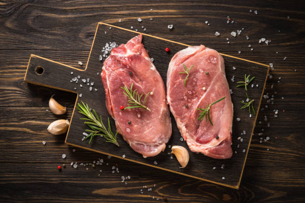 istock Fresh steaks with herbs and spices at wooden table. 1653021309