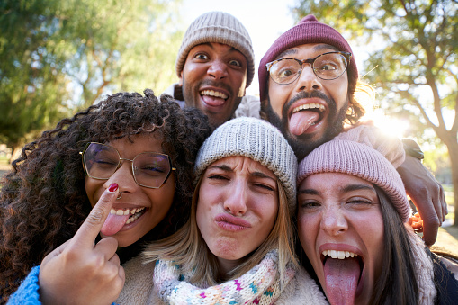 Winter selfie multiracial people together making funny faces in park. Group of young mixed race friends together having fun outdoor. Concept of friendship and lifestyle in millennial generation.