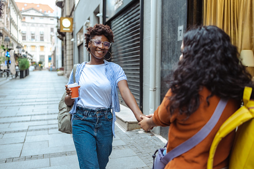 Two young friends with backpacks cheerfully walk on the street. They are on the city break