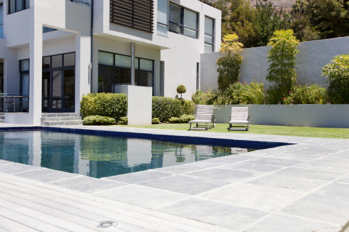Vertical view of swimming pool area in the garden of the house with wooden sun loungers and pool shutter in summer