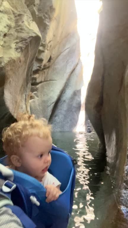 Baby in backpack carrier walking through canyon, fresh water running through