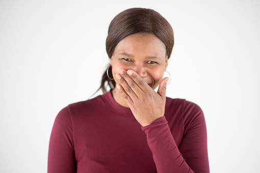 Confident African Woman studio portrait laughing shyly with hand on closed mouth
