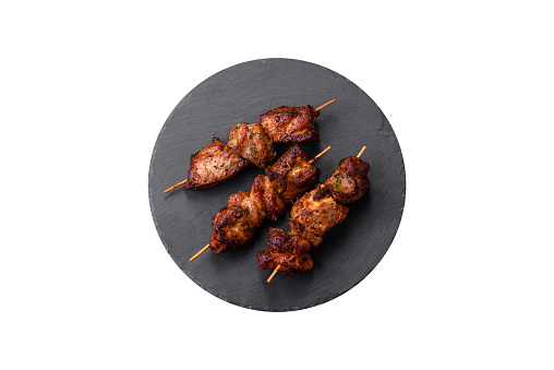 Delicious grilled chicken, turkey or pork skewers with salt, spices and herbs on a fire on a dark concrete background