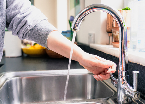 Close-up on the kitchen sink as a woman turns on the cold water tap in her home.
