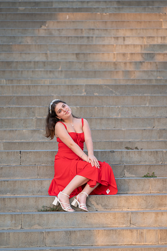Young girl in a red dress is sitting on the stairs.