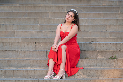 Thoughtful young women in a red dress is sitting on the stairs.